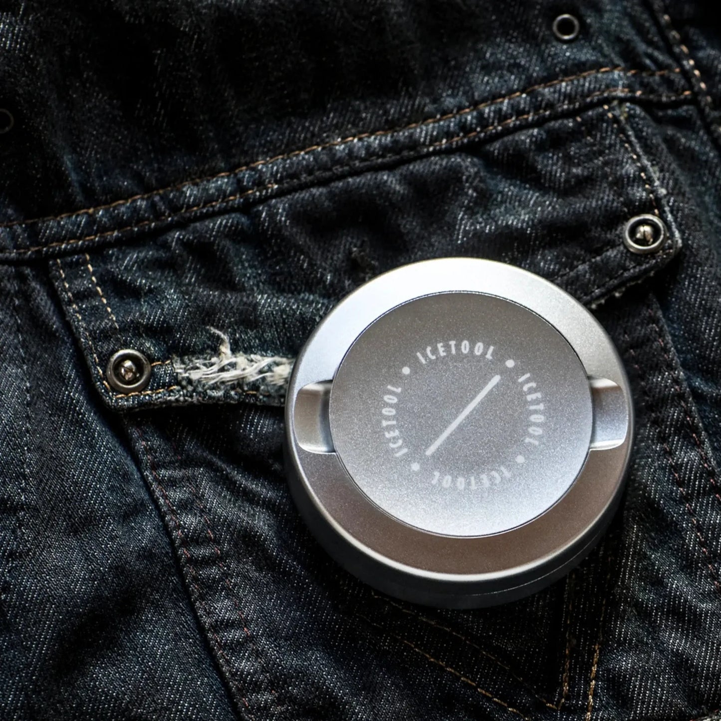 Metallic silver circular container with Icetool branding on a black denim background.