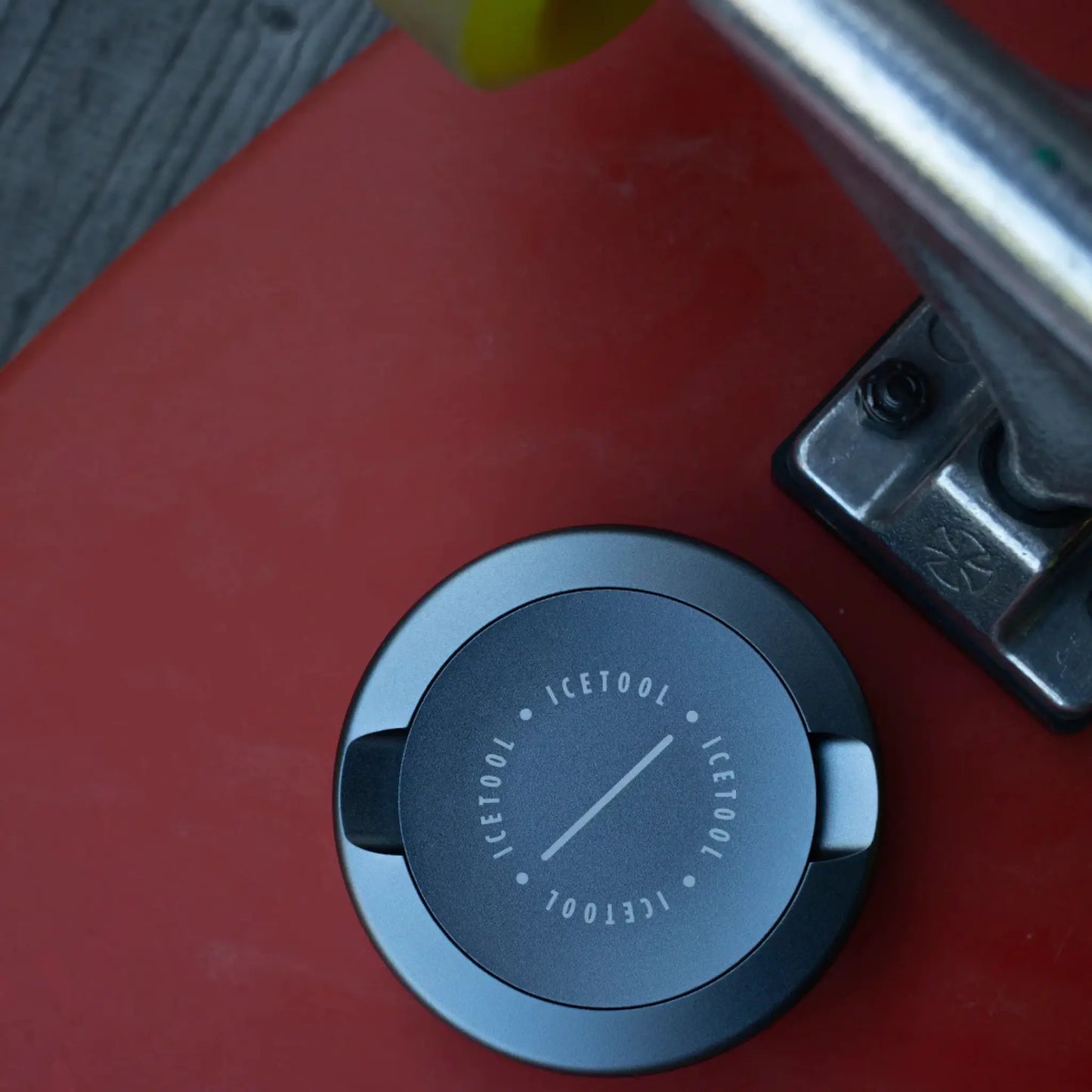 Round metallic container with Icetool branding laid on the underside of a red skateboard deck.