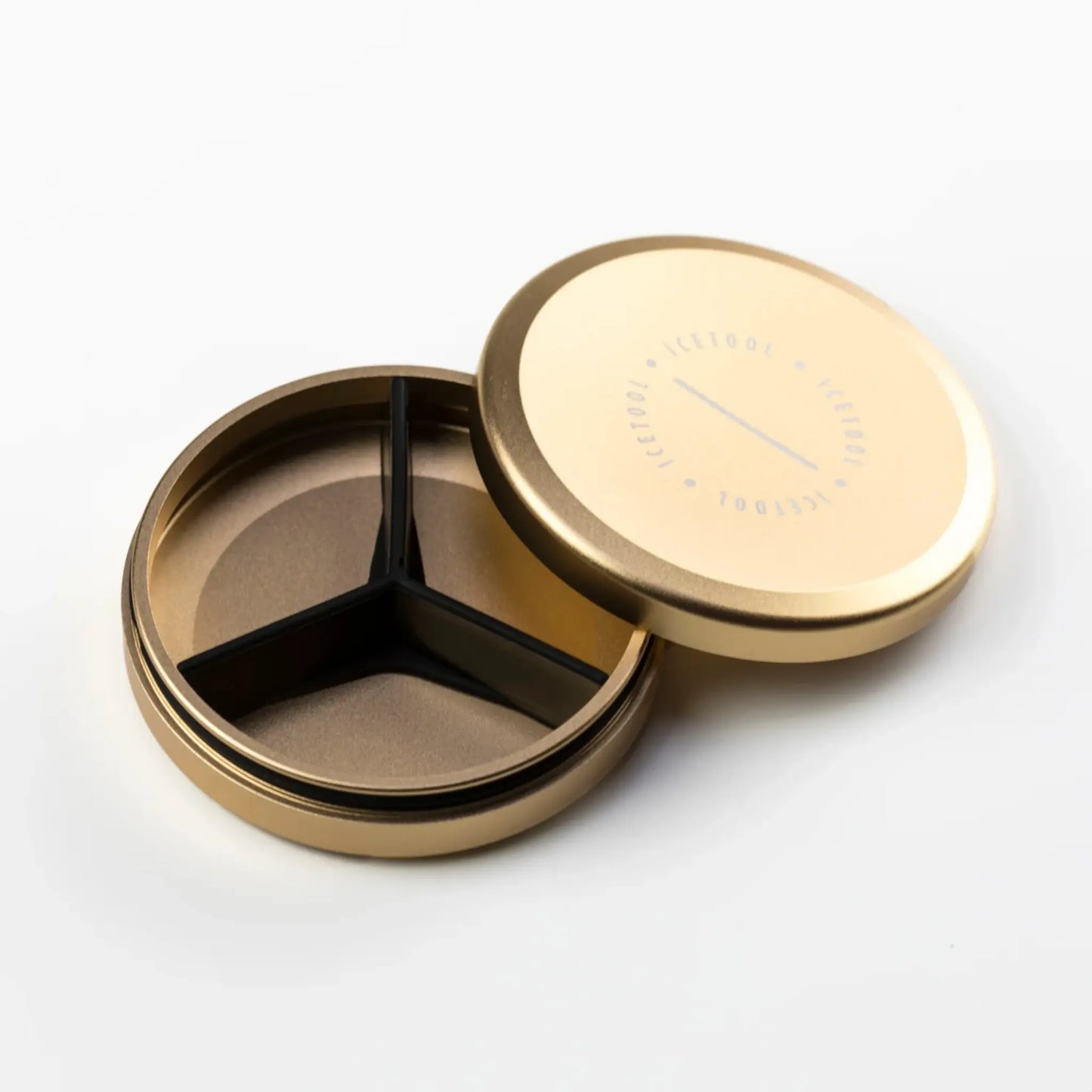Gold coloured round metal container with an open lid and black silicone separator inside.