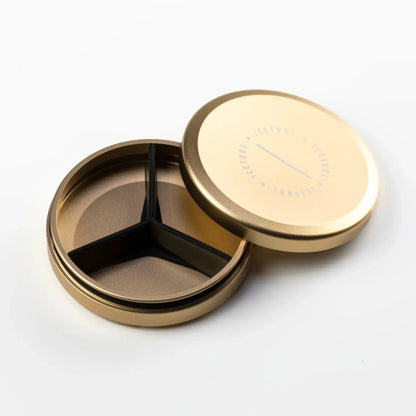 Gold coloured round metal container with an open lid and black silicone separator inside.